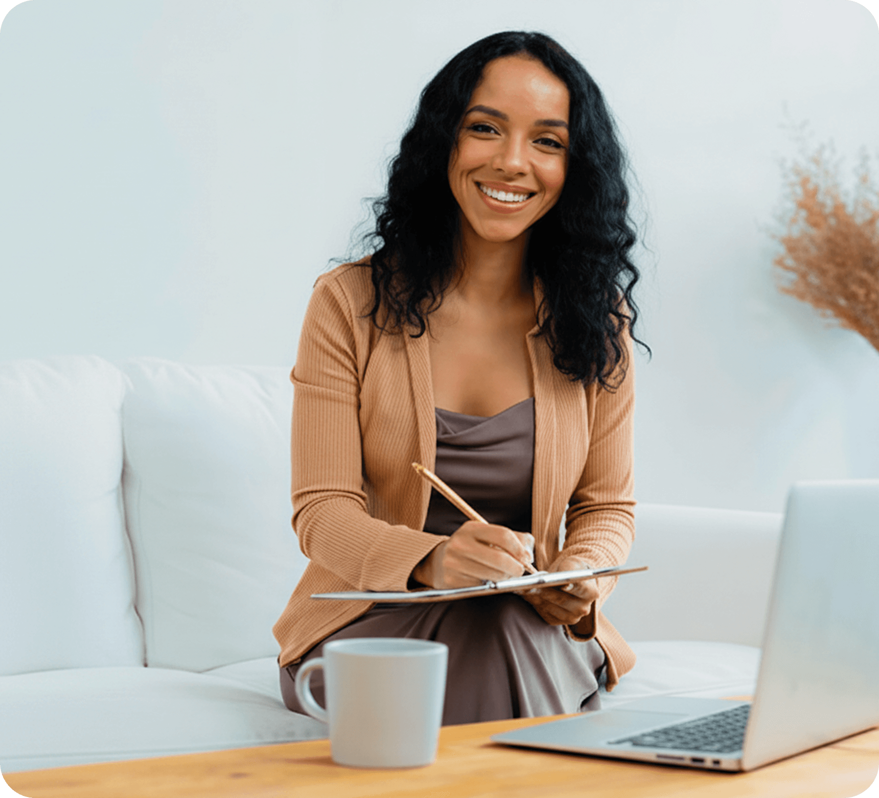 Professional smiling while writing notes with a laptop nearby