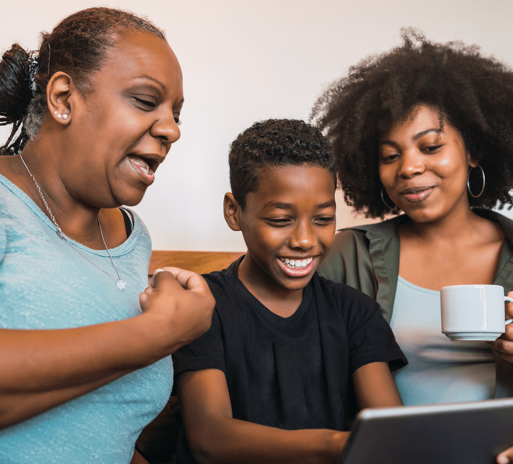 A grandmother, mother, and child smiling together while looking at a tablet
